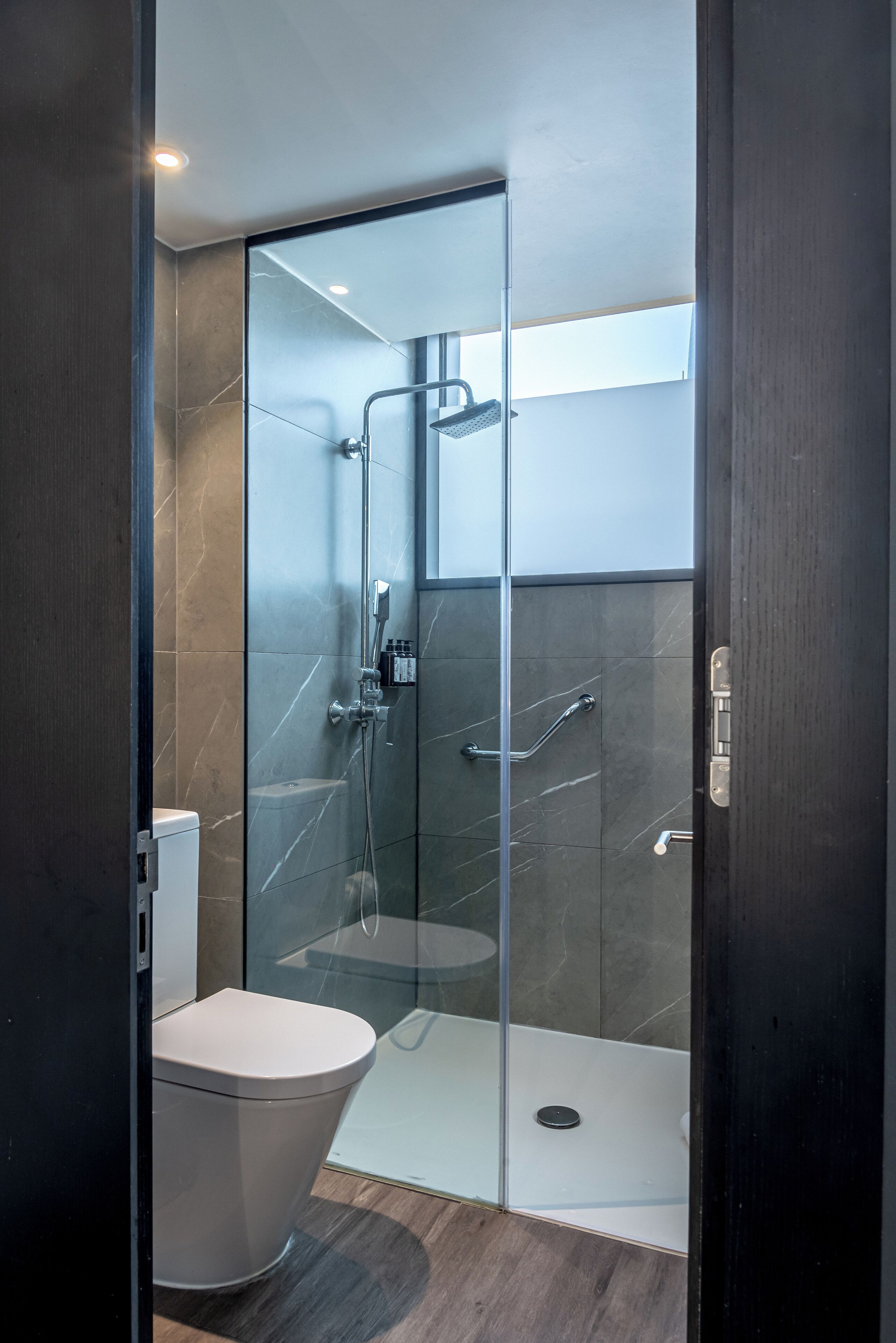 A modern bathroom with a glass-enclosed shower, a white toilet, and a dark wooden floor.