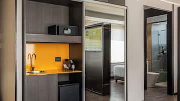 Quarto de hotel moderno com cozinha compacta, banheiro separado e área de estar.