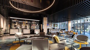 A modern lounge area with sofas and chairs, a bar with shelves, and large windows offering views.