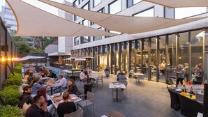 Un espace de restauration en plein air, avec des tables et des chaises, entouré de murs en verre et agrémenté d’une façade de bâtiment moderne.