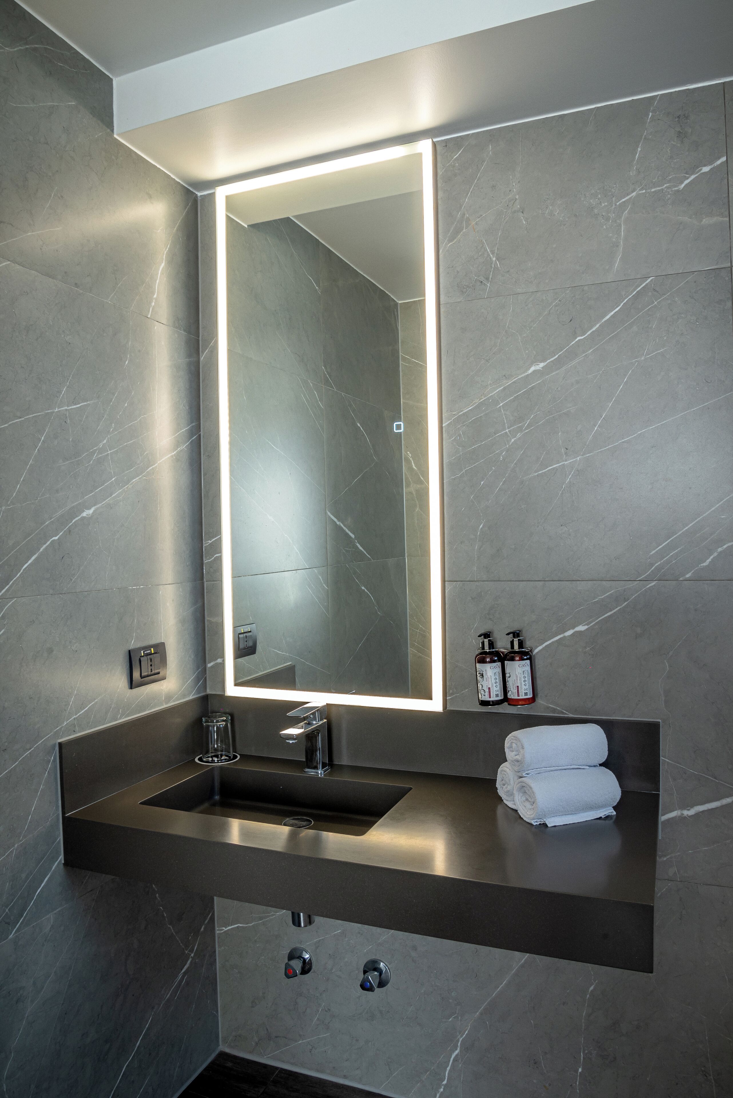 A modern bathroom with a large mirror, a sink, and two bottles of shampoo.