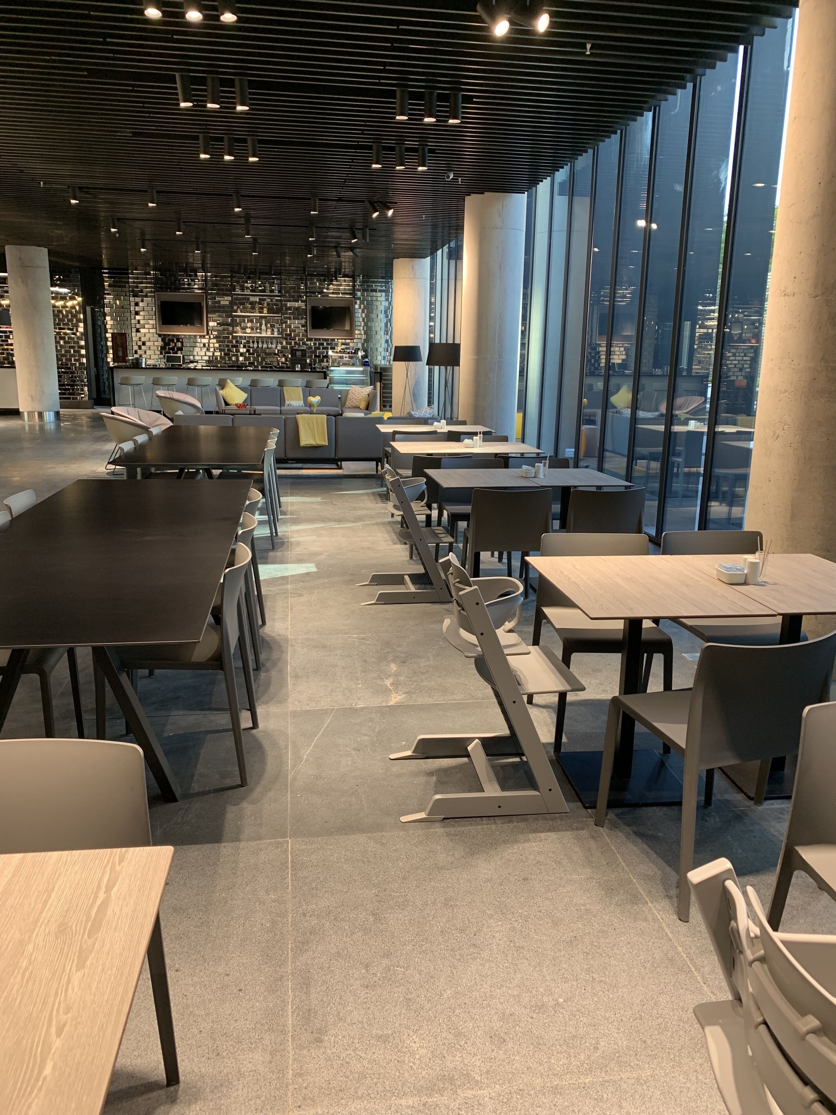 A modern restaurant with a long counter, seating area, and large windows offering a city view.