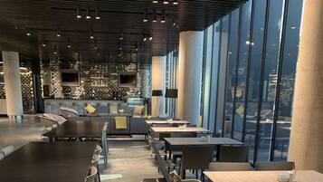 Un restaurante moderno con una barra alargada, zona de estar y grandes ventanales con vistas a la ciudad.