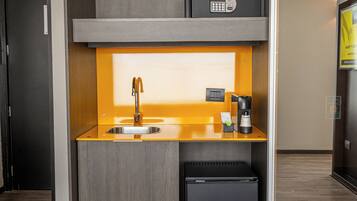Una kitchenette compacta con un lavamanos, una cafetera y un refrigerador pequeño.