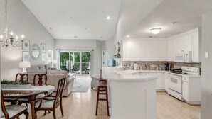 A spacious kitchen with white cabinetry, a central island, and a dining area with wooden chairs and a table. - Lake Norman Luxury Waterfront 3rd floor Condo with Elevator, Pool, Tennis (Cornelius)