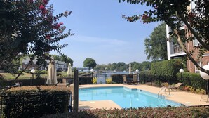 A swimming pool surrounded by greenery, with a view of a body of water and buildings in the background. - Lake Norman Luxury Waterfront 3rd floor Condo with Elevator, Pool, Tennis (Cornelius)