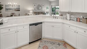 A modern kitchen with white cabinetry, a dishwasher, and a large window providing a view of the outdoors. - Lake Norman Luxury Waterfront 3rd floor Condo with Elevator, Pool, Tennis (Cornelius)