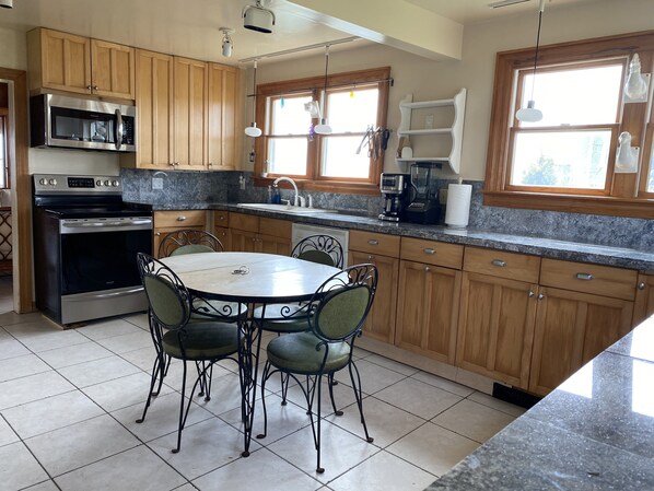 Una cocina con armarios de madera, electrodomésticos de acero inoxidable, una mesa de comedor con sillas y una ventana con cortinas.