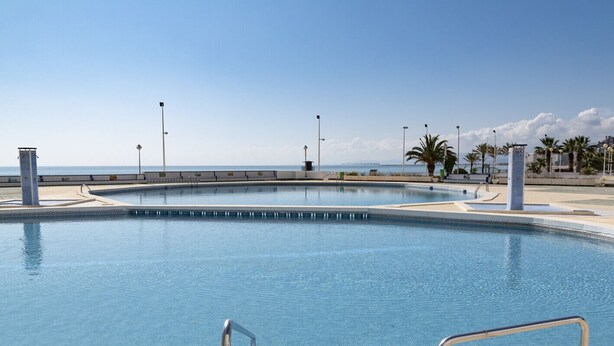 Una grande piscina vuota con acqua cristallina, circondata da un solarium in cemento e palme.