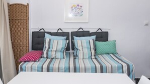 Un letto matrimoniale con biancheria a righe e due cuscini, un cesto in vimini e un quadro con fiori appeso al muro.