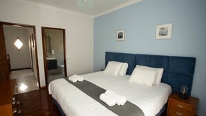 Een opgemaakt bed met witte lakens en een grijze accentkleur, een houten nachtkastje met een lamp en een blauw hoofdbord.