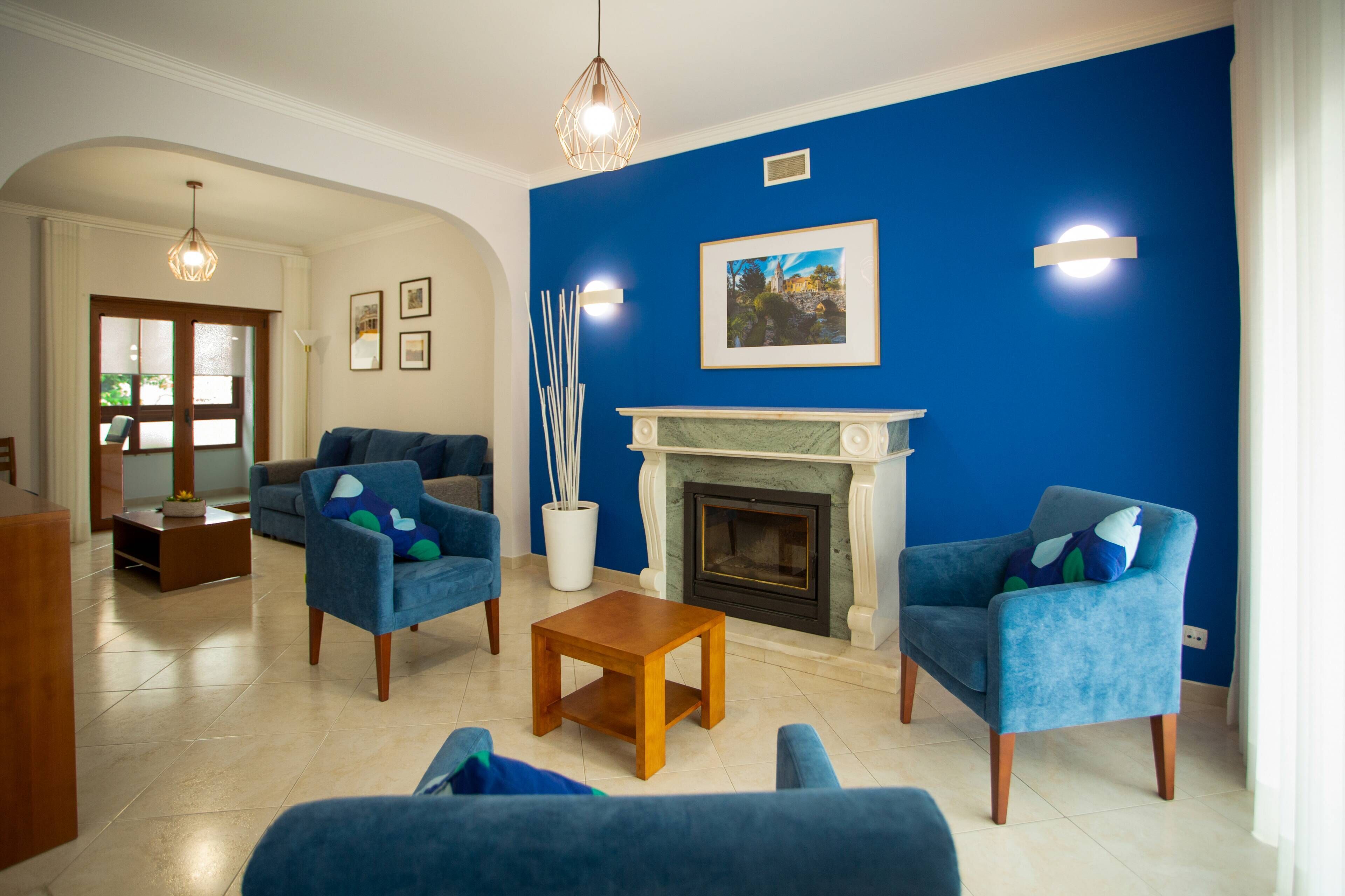 Un salon aux murs bleus, avec une cheminée et deux fauteuils bleus.