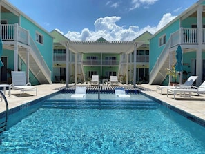 A swimming pool with lounge chairs and a covered seating area, surrounded by multi-story buildings with balconies.