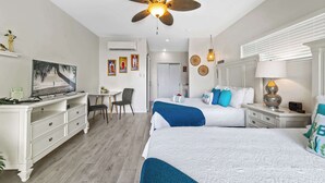 Habitación de hotel con dos camas, un escritorio con silla, un ventilador de techo y un televisor.