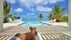 A poolside area with lounge chairs and umbrellas, overlooking a clear blue sea.