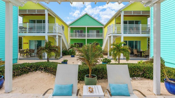 A hotel with a central green building flanked by two yellow buildings, each with balconies and outdoor seating. - The No Problem Ocean View Studio Cottage in East End (East End)