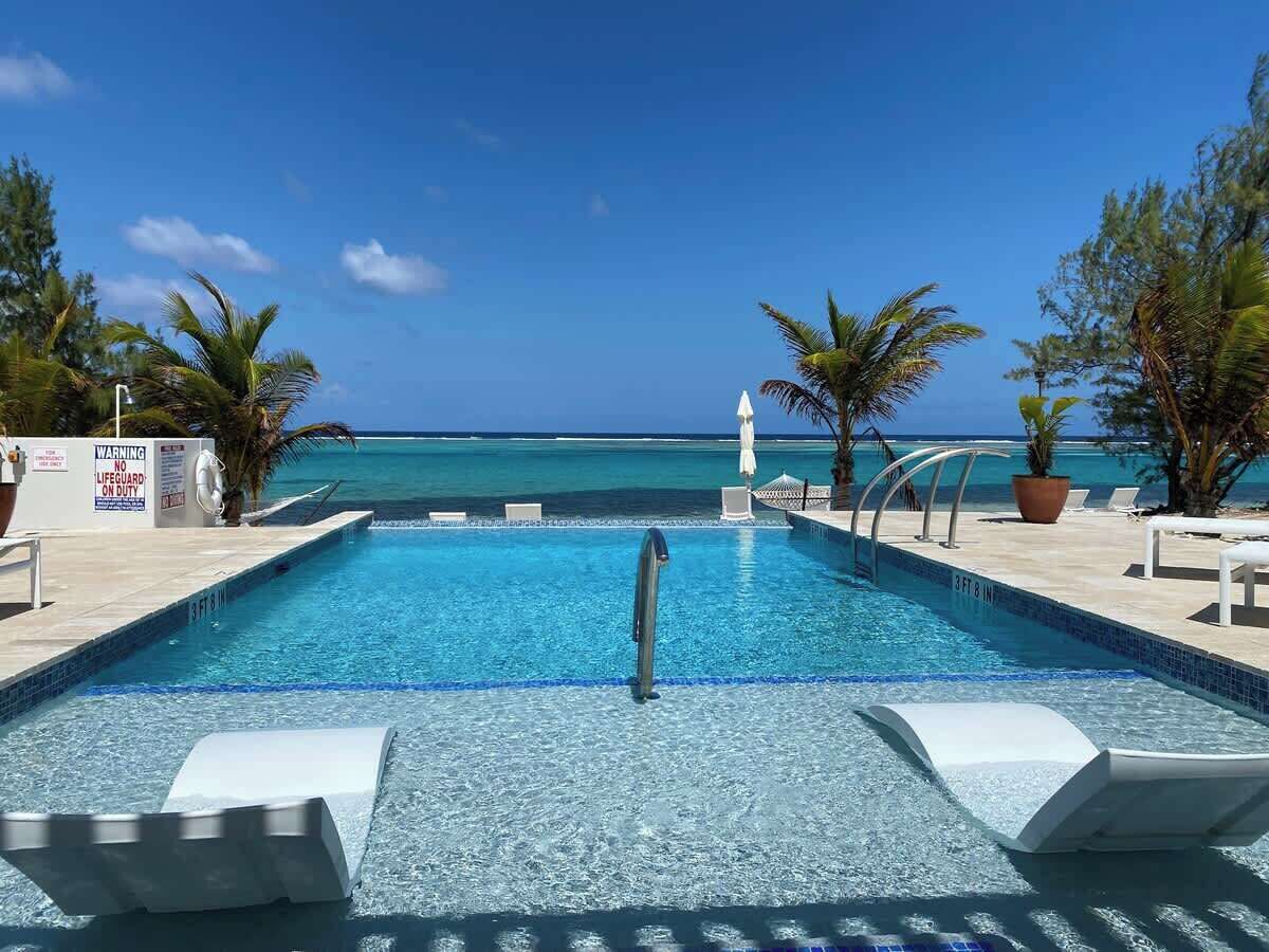 A pool with clear blue water, surrounded by lounge chairs and palm trees, with a view of the ocean.