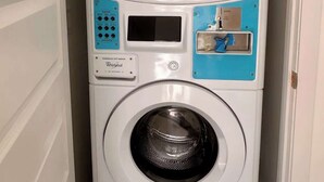 A compact, wall-mounted front-loading washer and dryer unit with a control panel and a water inlet. - The No Problem Ocean View Studio Cottage in East End (East End)
