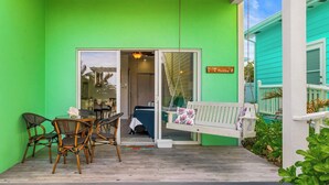 Un exterior verde brillante con un porche blanco, una hamaca y una zona de comedor con sillas y una mesa.