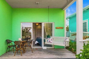 Un exterior verde brillante con un porche blanco, una hamaca y una zona de comedor con sillas y una mesa.
