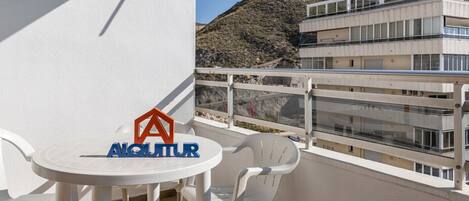A balcony with a table and chairs, a logo, and a view of a mountainous landscape.