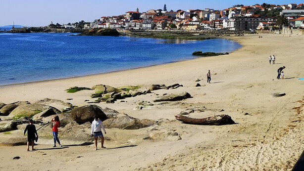 A beach with large rocks, a clear blue sea, and buildings in the background. - Casa Maria in Palmeira (Ribeira)