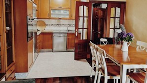 A kitchen with wooden cabinets, a dishwasher, and a dining area with a table and chairs. - Casa Maria in Palmeira (Ribeira)