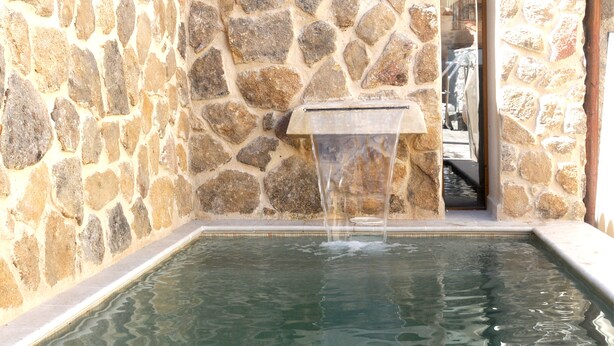 Un muro de piedra con una fuente, una piscina y vistas despejadas del interior.