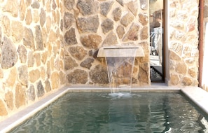 Un muro de piedra con una fuente, una piscina y vistas despejadas del interior.