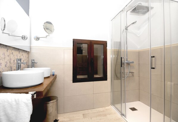 A modern bathroom with two sinks, a mirror, a shower enclosure, and a trash bin.