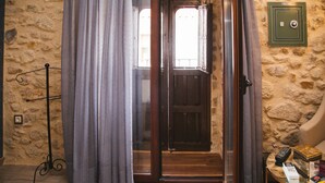 Interior con pared de piedra, una puerta de madera, un perchero metálico y una pequeña mesa con un control remoto y libros.