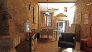 Un interior acogedor con pared de ladrillo, una zona de comedor con mesa y sillas, un sillón negro y un sofá rojo.