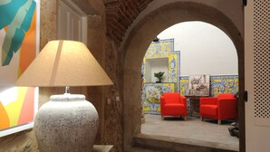 Una habitación con una lámpara de piedra, vista a través de un arco hacia una zona de estar con sillas rojas, y una pared de azulejos con diseños azules y amarillos.