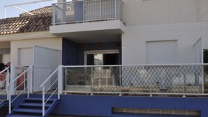 Un immeuble de deux étages avec une façade bleue, un balcon doté d’une rambarde en métal et un escalier menant à l’entrée.