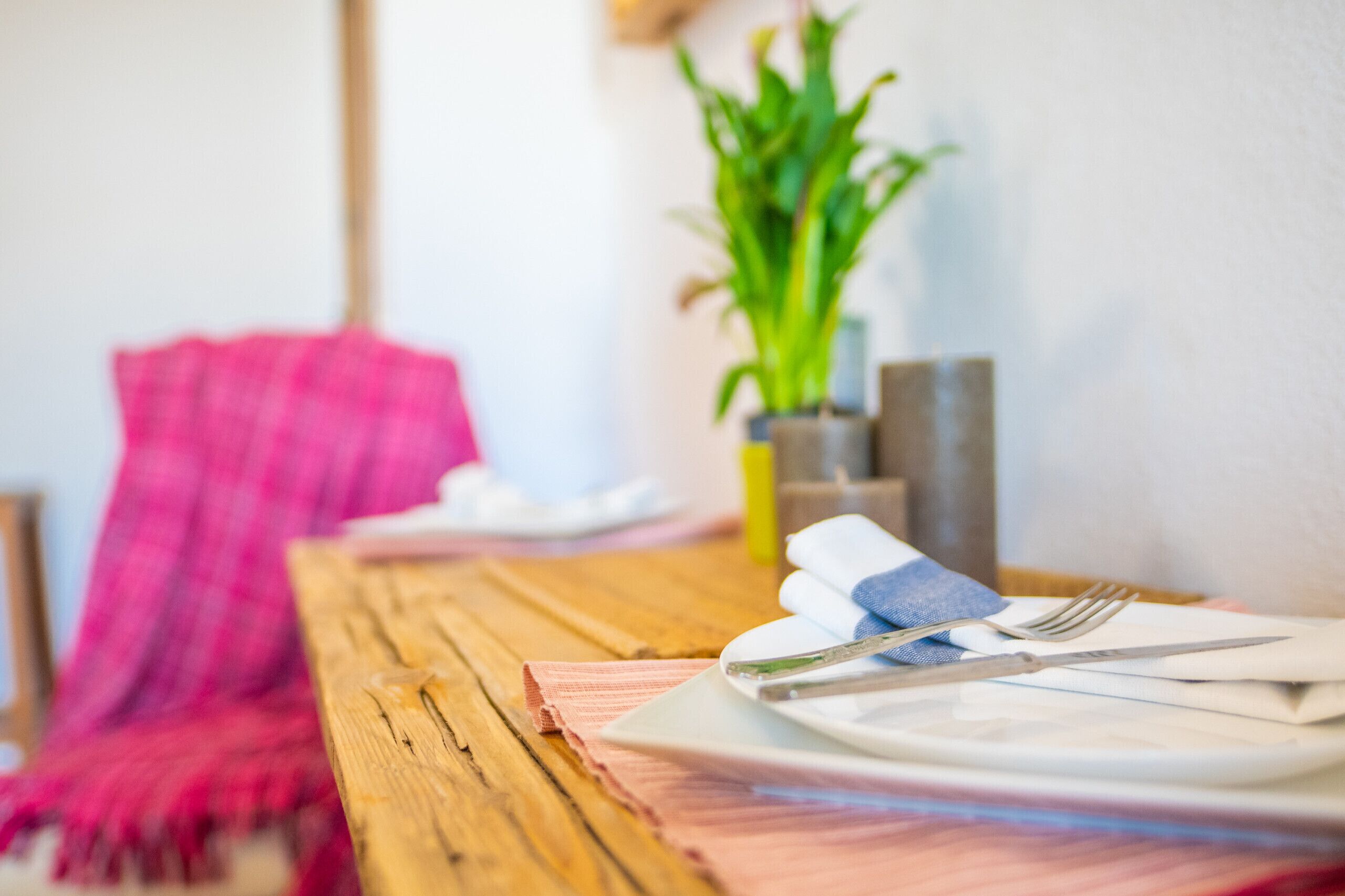 Una mesa de madera con un mantel impecable, una servilleta doblada, un plato, un tenedor y un cuchillo.