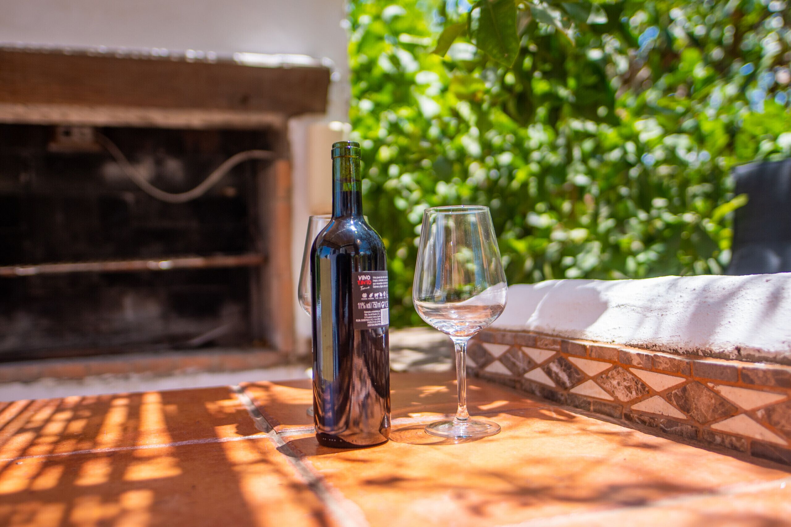 A bottle of wine and an empty glass on a tiled table outdoors.