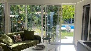 Un salon moderne avec un canapé vert, une table basse blanche et une vue sur un jardin avec une piscine.