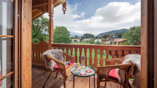 Eine Holzterrasse mit Korbstühlen und einem Tisch, mit Blick auf eine reizvolle Landschaft mit Häusern und Bäumen.