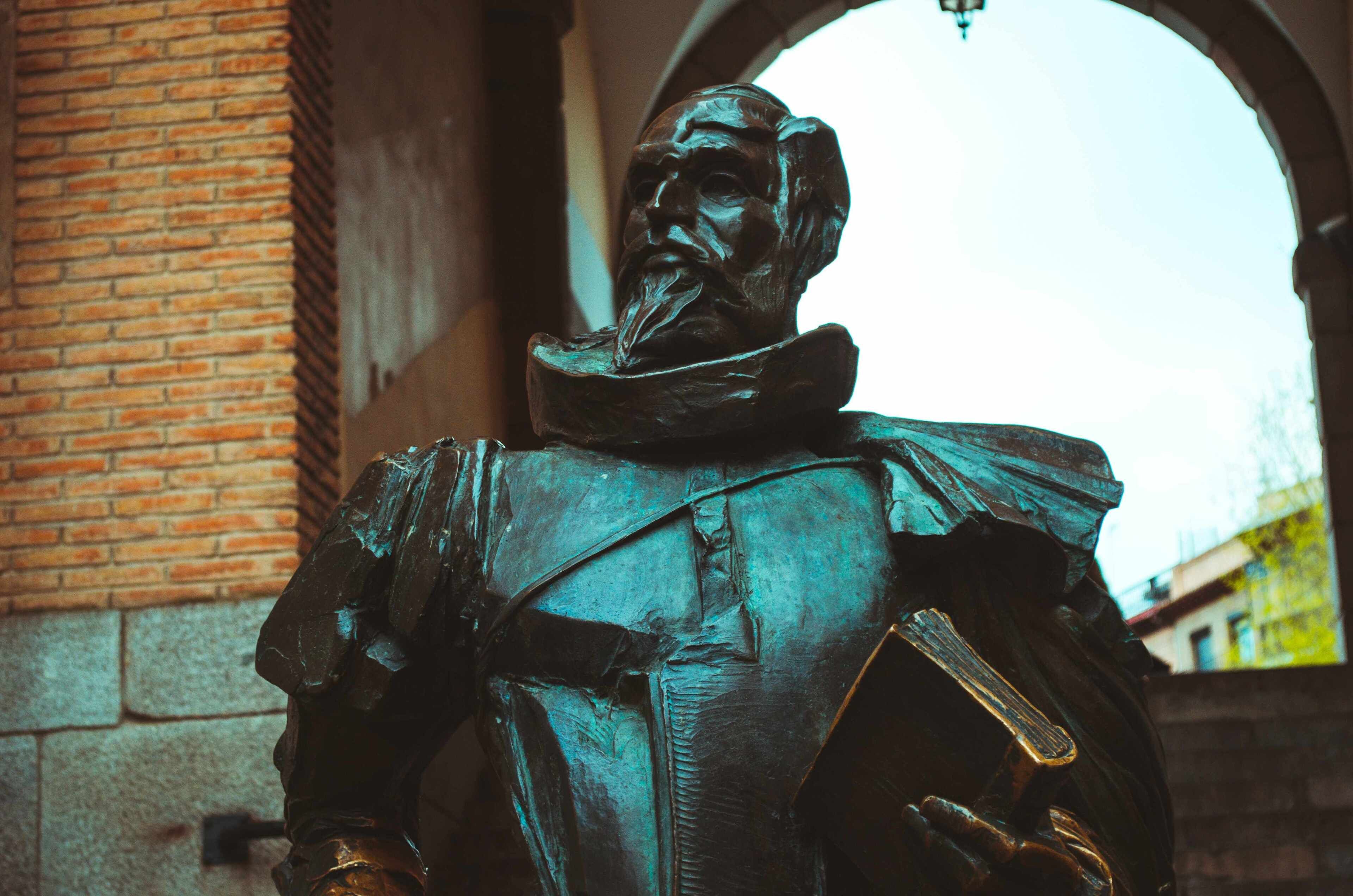A statue in an outdoor setting with a brick wall and an archway in the background.
