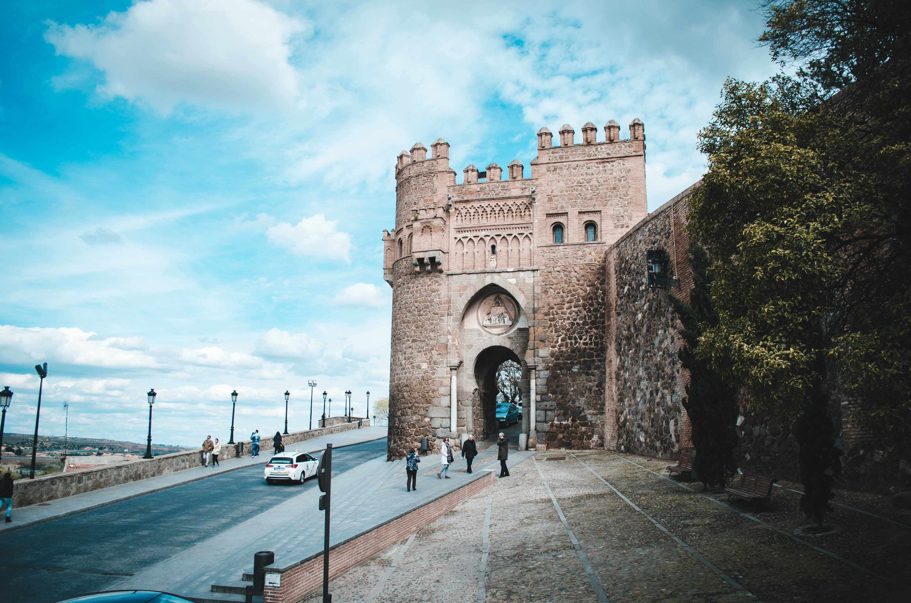 Una antigua puerta de piedra con arco, un camino empedrado y vistas del paisaje circundante.