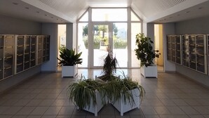 Eine großzügige Lobby mit einer zentralen Pflanzengruppe, großen Fenstern und Ablusclockern an den Wänden.