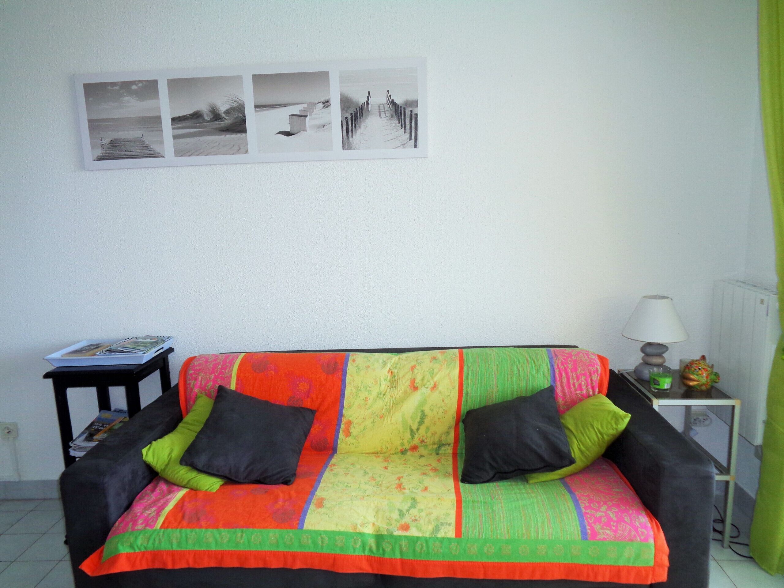A room with a colorful sofa, a small table with a lamp, and a wall with three black and white photographs.