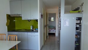 Eine kompakte Küche mit Essbereich, ein Bett im angrenzenden Zimmer und ein Kühlschrank mit Kaffeemaschine.