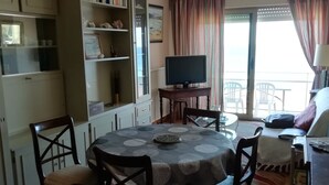 A dining area with a round table, chairs, and a television on a stand. There are bookshelves and a cabinet with a television on top. - Ocean View!! One-bedroom apartment with a garage!! "Mobility Lease" rental. (Saint-Malo)