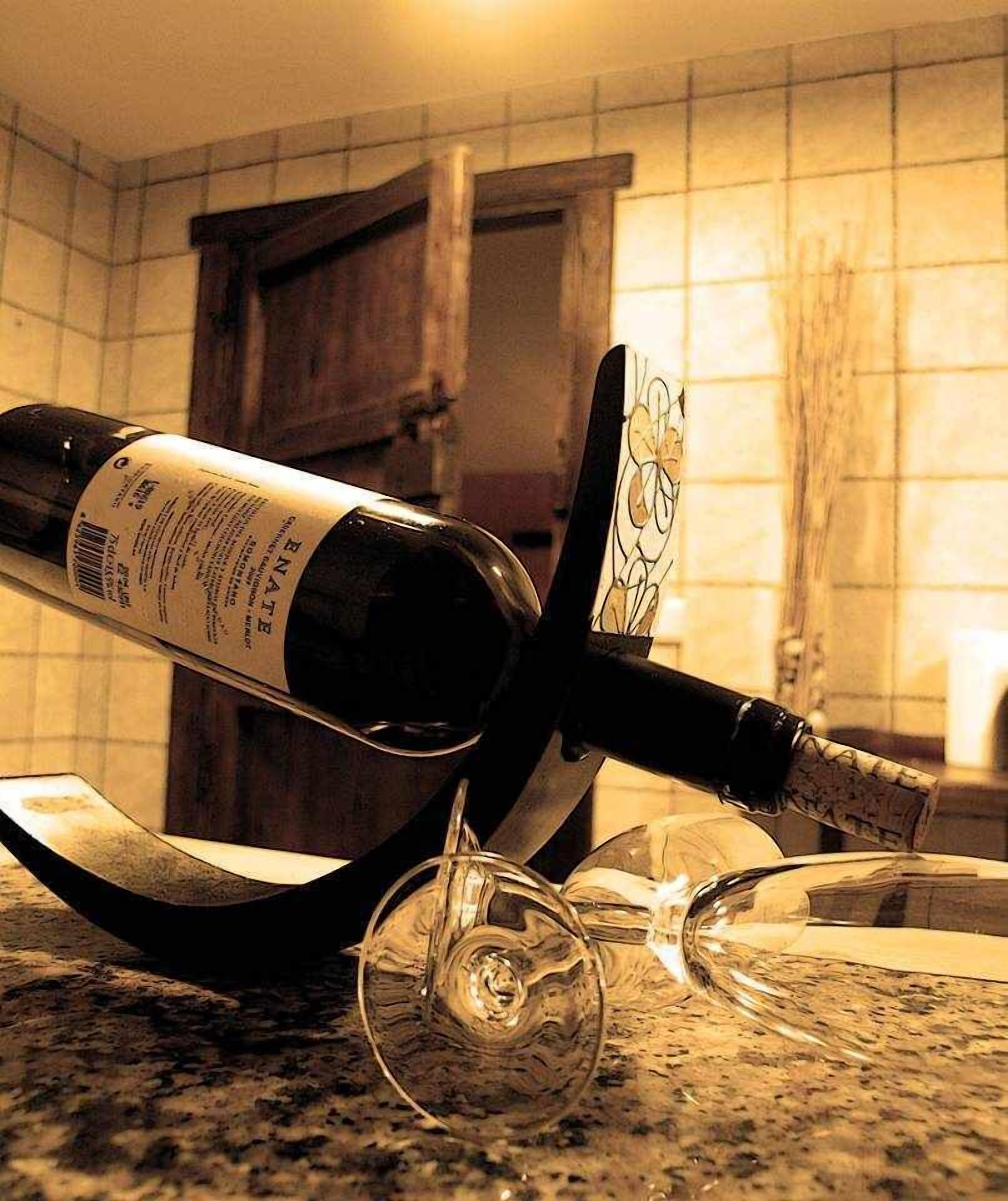 A bottle of wine on a counter with a glass and a corkscrew.