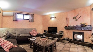 Una sala de estar con sofá, televisor, chimenea y piso de baldosas de piedra.