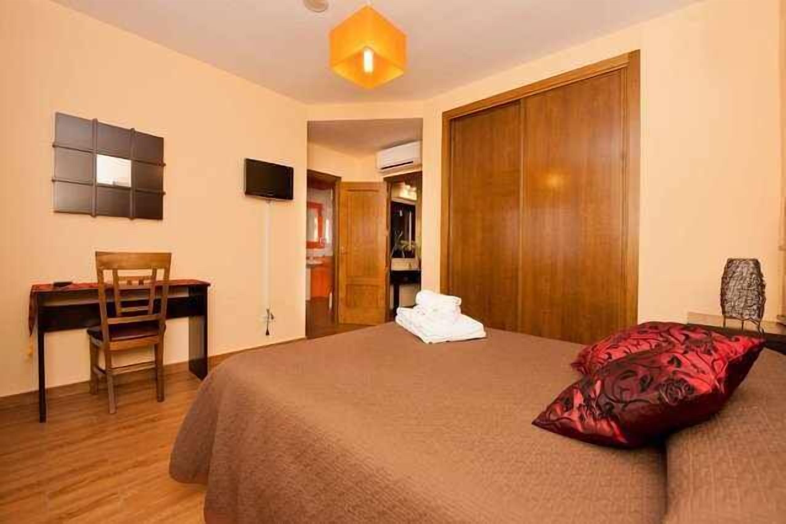 A bedroom with a bed, a desk, a chair, a wardrobe, and a television.