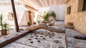 Un banco de madera rústico con remaches metálicos, ubicado en un patio con paredes de piedra y techo de tejas.