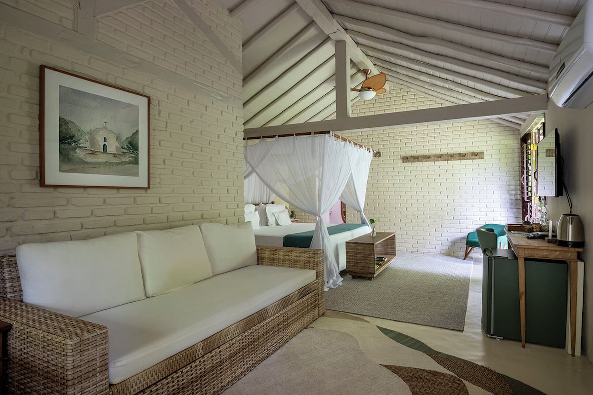 Una habitación con pared de ladrillo blanco, una cama con dosel, un sofá, una mesita y un televisor.