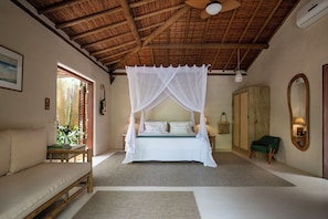 A room with a bed under a canopy, a sofa, a chair, a mirror, and a wardrobe.